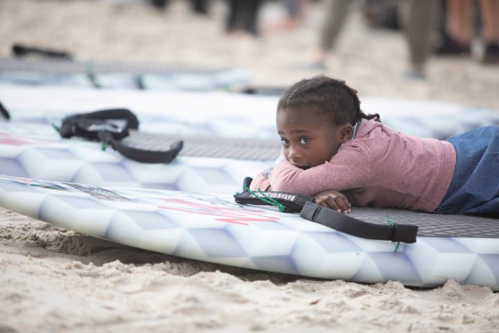 Noluthando Makalima's daughter Iminathi, lies on her mother's surf board at Muizenberg beach, Cape Town, on Saturday 8 May 2021. (Photo: Leila Dougan)