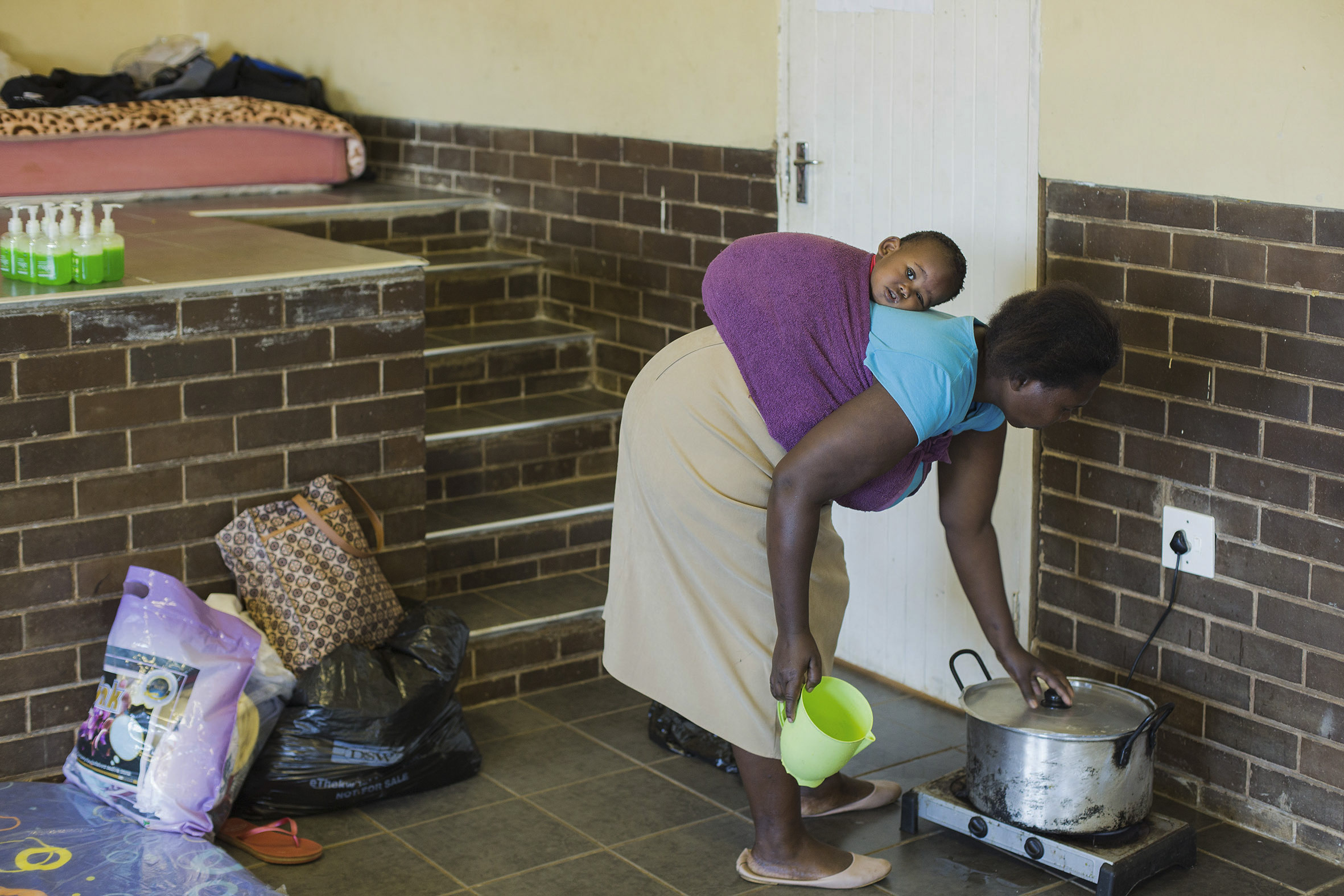 Flood victims - a woman carrying a baby on her back cooks steam bread at the community hall