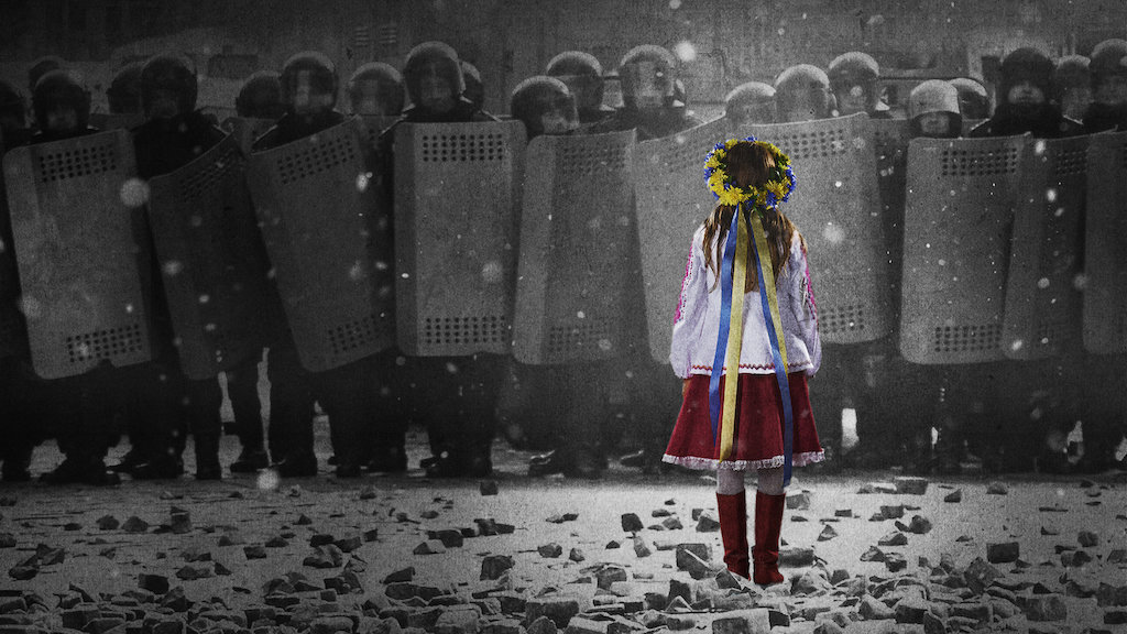 A girl in traditional dress stands in the snow in front of a police barricade.