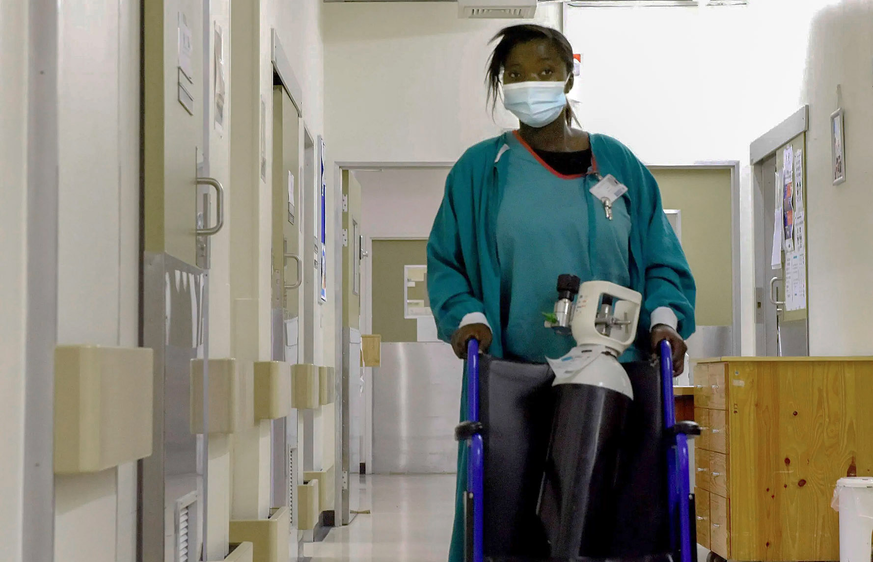 A nurse wheels an oxygen tank through a hospital hallway