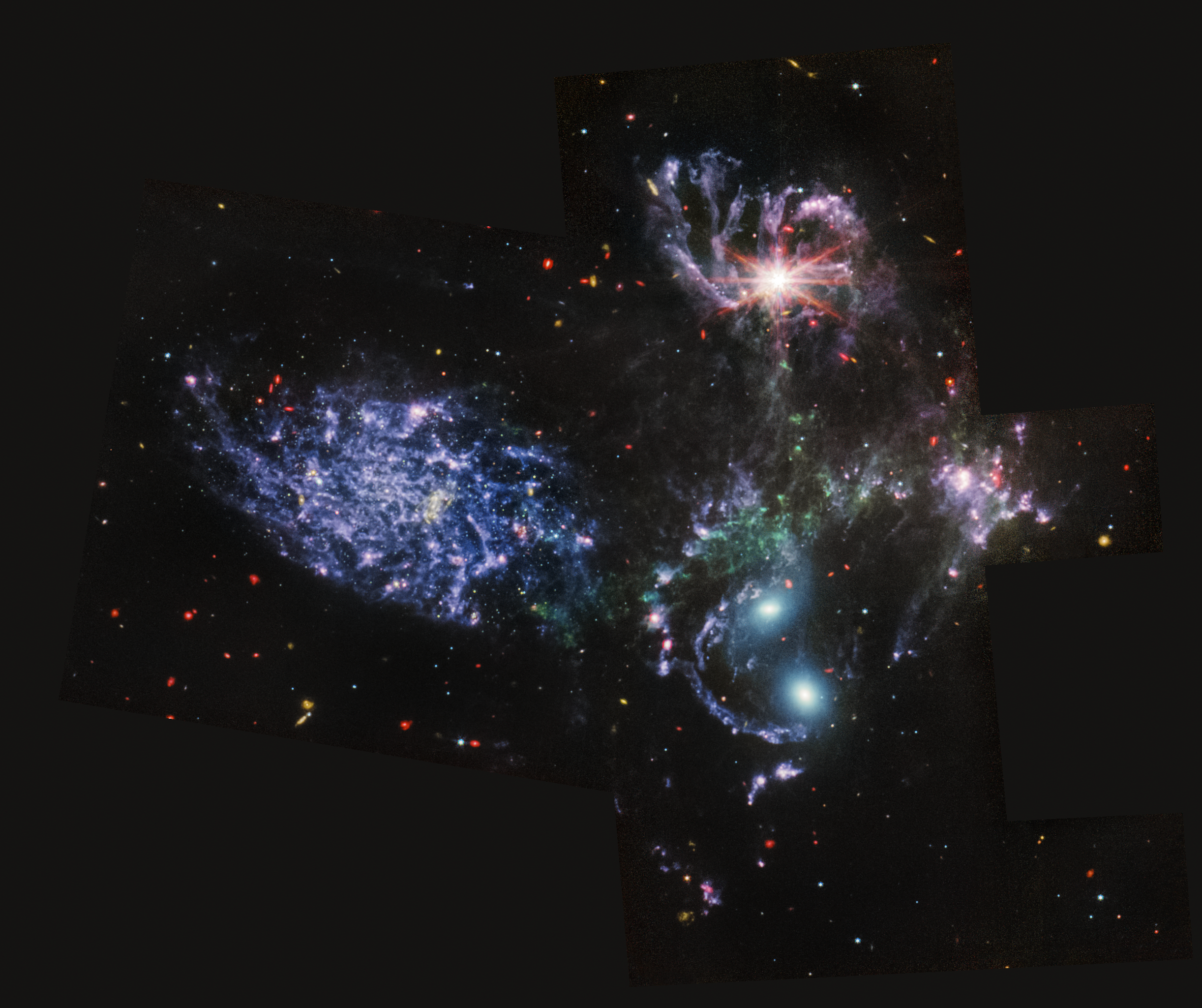 Image of a group of four galaxies that appear close to each other in the sky: two in the middle, one toward the top, one to the upper left. In addition, there is a large bright patch toward the right. The galaxy at the top has a bright reddish core and is surrounded by swirls of blue and purple filaments that travel inward to its bright core, also highlighted by eight diffraction spikes. The galaxy on the left is a mass of purple gas surrounding a dim red core. The mass is made from small clumps, each slightly illuminated. The two galaxies in the middle have two bright, blue cores, surrounded by purple wisps. The bright patch to the right is made from clouds of blue and purple, strung together in filament-like bands. Surrounding the galaxies is a background peppered with red, blue, and purple dots, which are distant stars and galaxies.