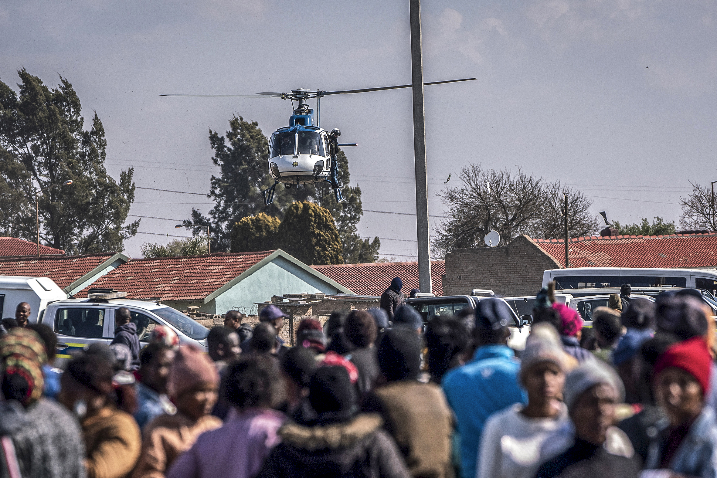 A police helicopter is seen hovering above a crowd of residents