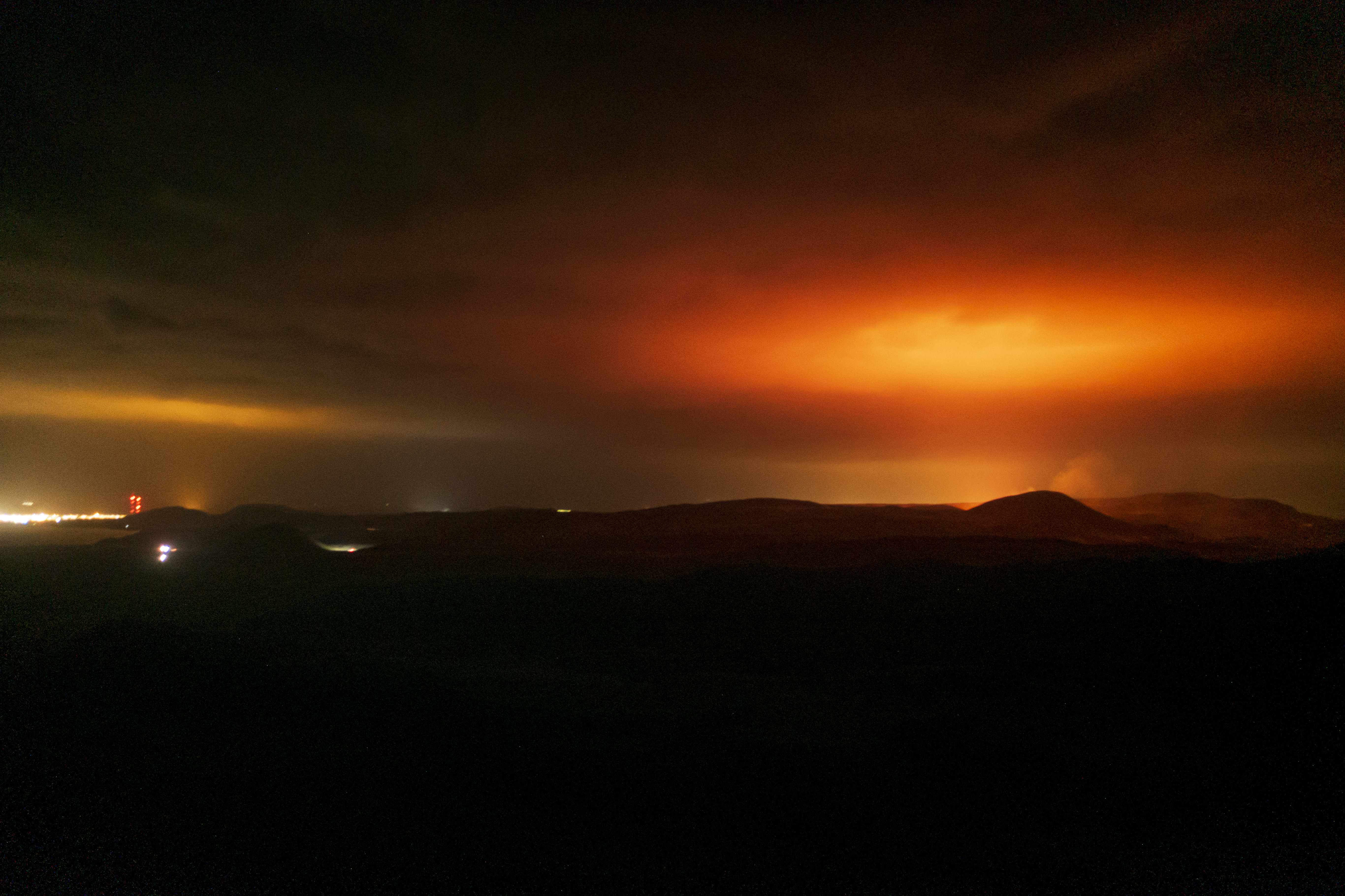 The red glare from the volcano eruption lights the night sky over Grindavik (L) on the Reykjanes Peninsula, Iceland, early 20 March 2021 (picture taken with a drone). A volcanic eruption at Geldingadalur, close to Fagradalsfjall, shattered Iceland in the night of 19 to 20 March 2021 following a series of small quakes, monitored and documented by the Islandic Meteorological Office (IMO). EPA-EFE/GOLLI / ICELANDREVIEW 