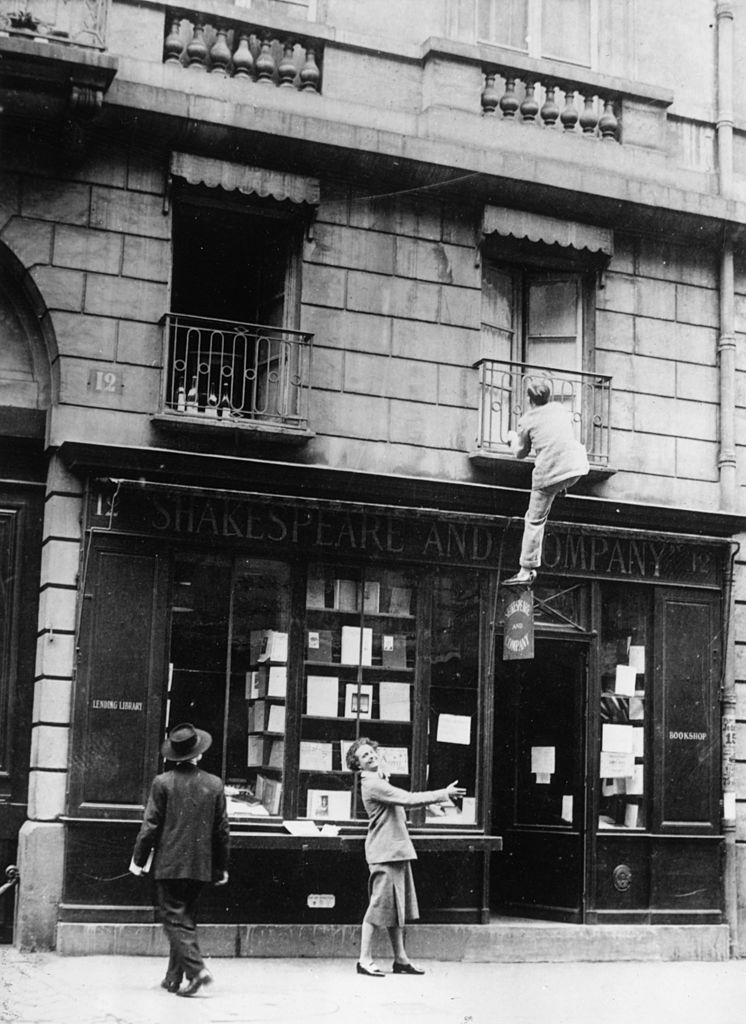 circa 1935: Sylvia Beach (1887 - 1962), unofficial historian of 'The Lost Generation' watches composer George Antheil (1900 - 1959) climbing up to a second floor window of her bookshop, 'Shakespeare and Company', 12 Rue de l'Odeon, Paris. She was the first bookseller to sell copies of James Joyce's 'Ulysses' which was printed in France. (Photo by Paul Almasy/Three Lions/Getty Images)