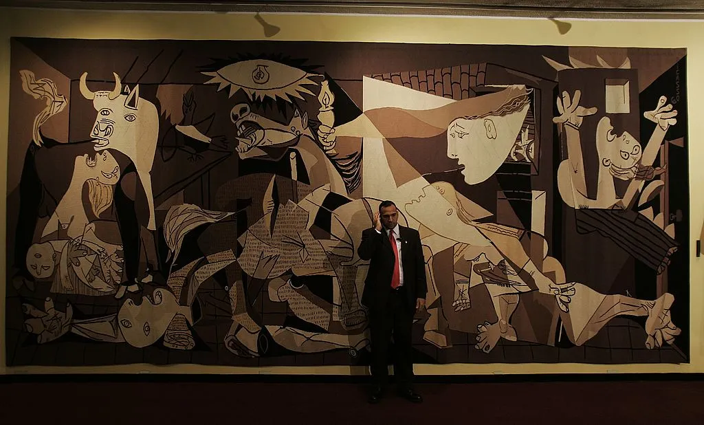 NEW YORK - MAY 12: A member of the security detail for John Bolton, the United States Ambassador to the United Nations, speaks on his radio in front of a reproduction of the Pablo Picasso painting "Guernica" May 12, 2006 at the United Nations headquarters in New York. The United Nations headquarters, completed in 1952, is widely considered to be a landmark achievement of the International Style of architecture, a style that reached a massive climax with the construction of the World Trade Center 20 years later. (Photo by Chris Hondros/Getty Images)