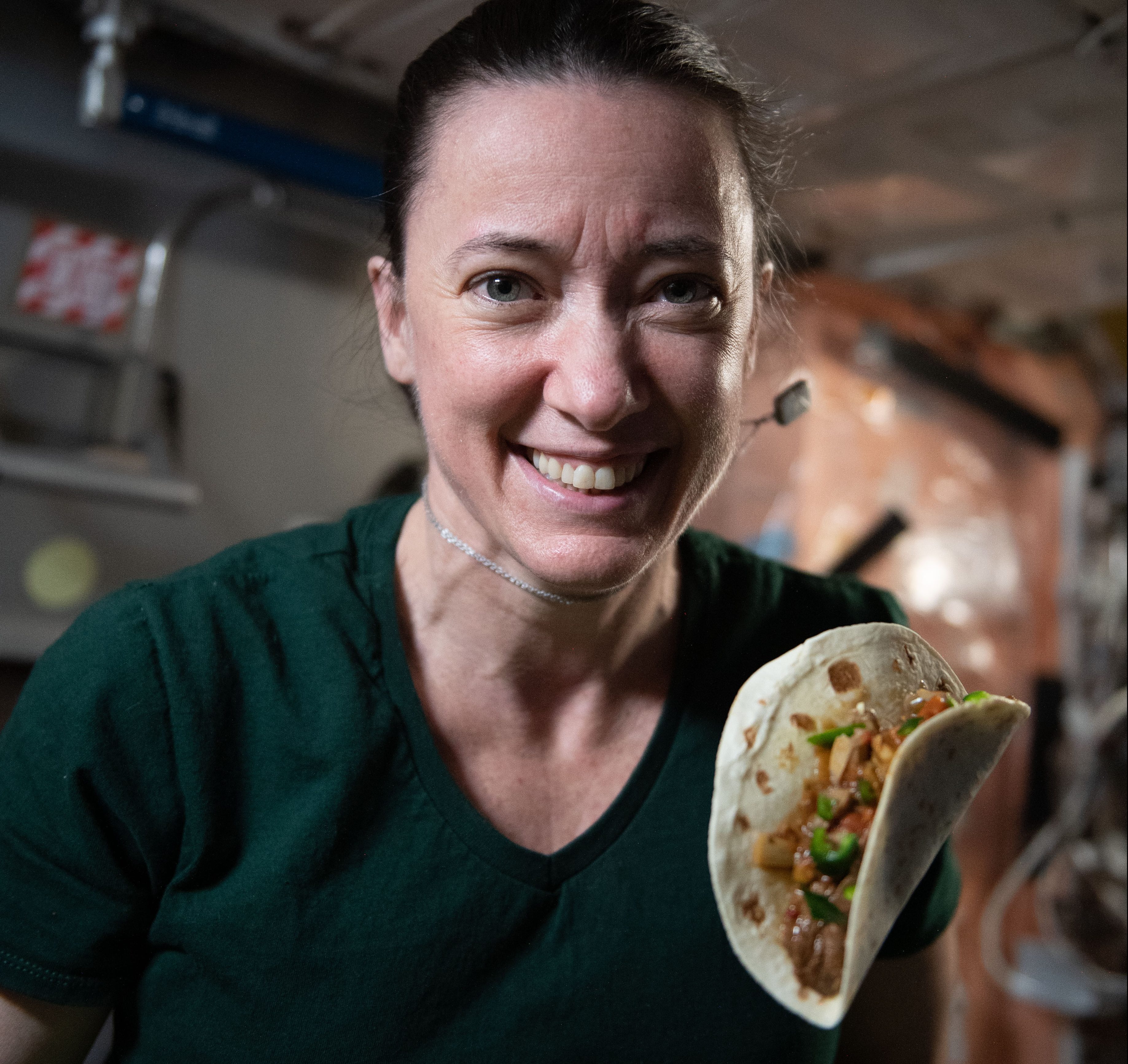 iss066e023198 (October 29, 2021) -- NASA astronaut and Expedition 66 flight engineer Megan McArthur is seen with a taco made using fajita beef, rehydrated tomatoes and artichokes, and chile peppers. The chile peppers were grown as part of the Plant Habitat-04 investigation aboard the International Space Station. The crop started growing on July 12, 2021, and represent one of the longest and most challenging plant experiments attempted aboard the orbiting laboratory. The chile peppers started growing on July 12, 2021, and represent one of the longest and most challenging plant experiments attempted aboard the orbiting laboratory. NASA astronaut and Expedition 66 flight engineer Mark Vande Hei conducted the first harvest of the pepper crop on October 29, 2021. Crew members sanitized the peppers and completed a scientific survey after their taste test. The Crew-3 astronauts will take over the crop when they arrive at the orbiting laboratory, and will conduct a final harvest of the peppers in late November. They will also sanitize and sample the crop, and complete surveys. Some peppers and their leaves from the final harvest will return to Earth for further analysis. What we learn will inform future crop growth and food supplementation activities for deep space exploration.