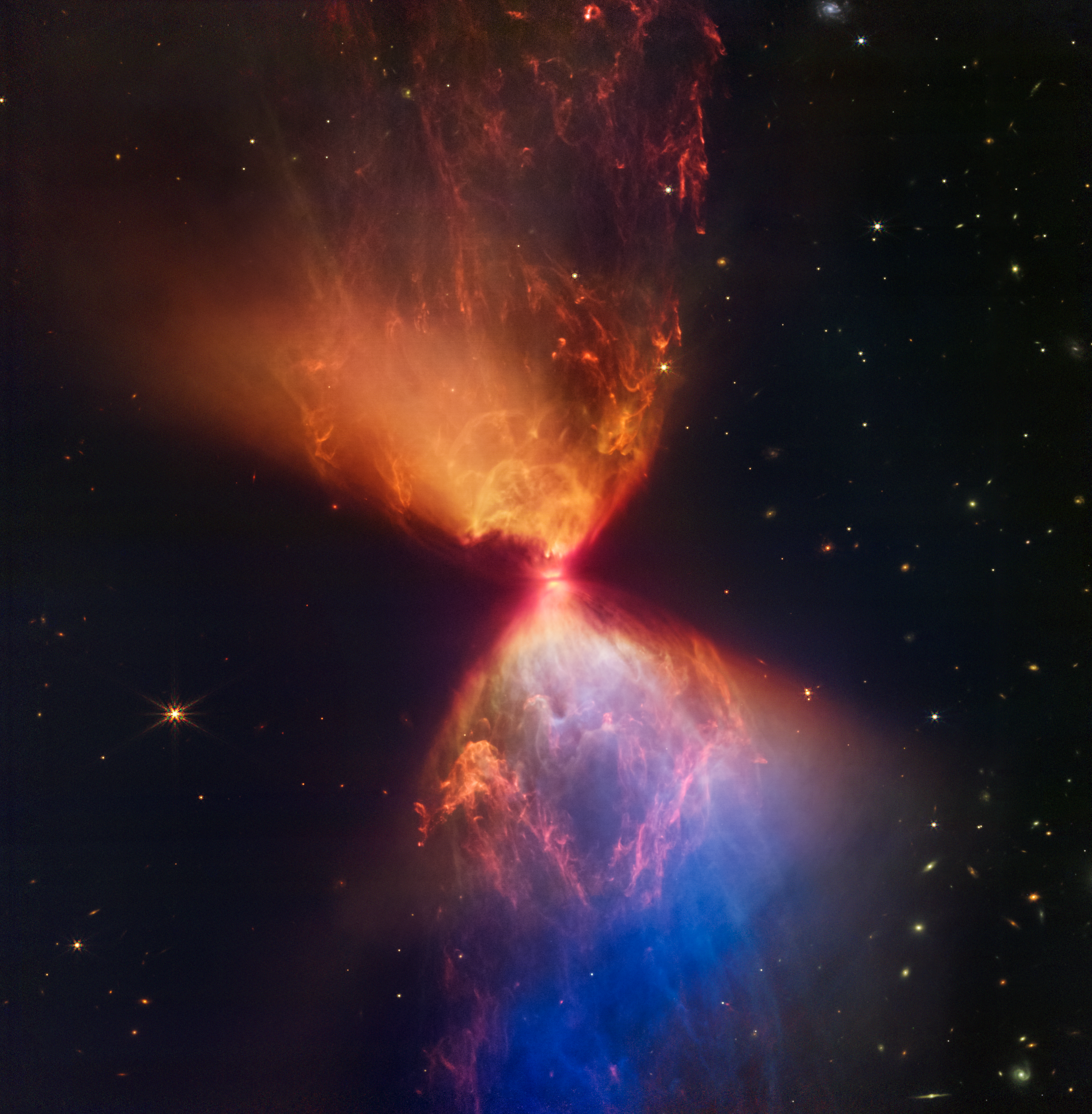 The protostar within the dark cloud L1527, shown in this image from NASA’s James Webb Space Telescope Near-Infrared Camera (NIRCam), is embedded within a cloud of material feeding its growth. Ejections from the star have cleared out cavities above and below it, whose boundaries glow orange and blue in this infrared view. The upper central region displays bubble-like shapes due to stellar “burps,” or sporadic ejections. Webb also detects filaments made of molecular hydrogen that has been shocked by past stellar ejections. The edges of the cavities at upper left and lower right appear straight, while the boundaries at upper right and lower left are curved. The region at lower right appears blue, as there’s less dust between it and Webb than the orange regions above it. Image: NASA, ESA, CSA, STScI / Joseph DePasquale (STScI), Alyssa Pagan (STScI), Anton M. Koekemoer (STScI)