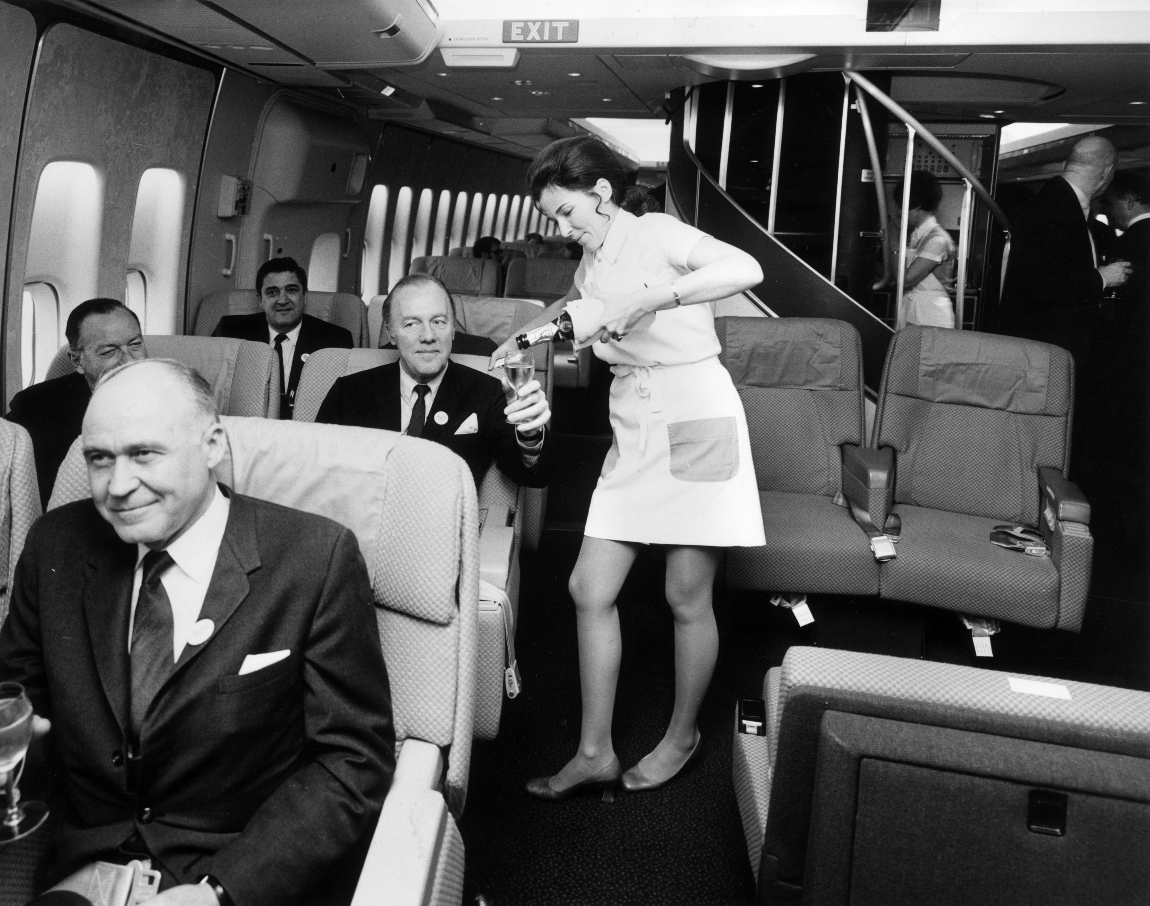 A Pan American (Pan Am) airhostess serving champagne in the first class cabin of a Boeing 747 jumbo jet. Image: Tim Graham / Getty Images