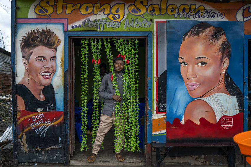 Jean Claude (27) poses in front of his hairdressing salon in Goma, Democratic Republic of Congo, 26 November 2022. On the N2 highway leading north out of Goma in the Democratic Republic of Congo, colourful hair salon storefronts hide interiors full of customers. The customers are mostly women who are ready to spend their entire day getting the perfect hairstyle, whether it’s butterfly or tribal braids, or curly hair twists. Yet while most of the work is performed by women, it seems that the salons are owned by men, some as young as 20 years old. At a time of tension and economic uncertainty, the bold names and brightly coloured storefronts bring a sense of normalcy to residents who have contended with conflict and natural disasters for decades. The Salon Mixte, the Clinique de Beauté, the Just Love salon and the Salon King are all open for business and here to stay. Despite fighting between M23 rebels and FARDC government forces north of Goma, life goes on for residents of the lakeside town. © Jerome Delay, France, Shortlist, Professional competition, Portraiture, Sony World Photography Awards 2023