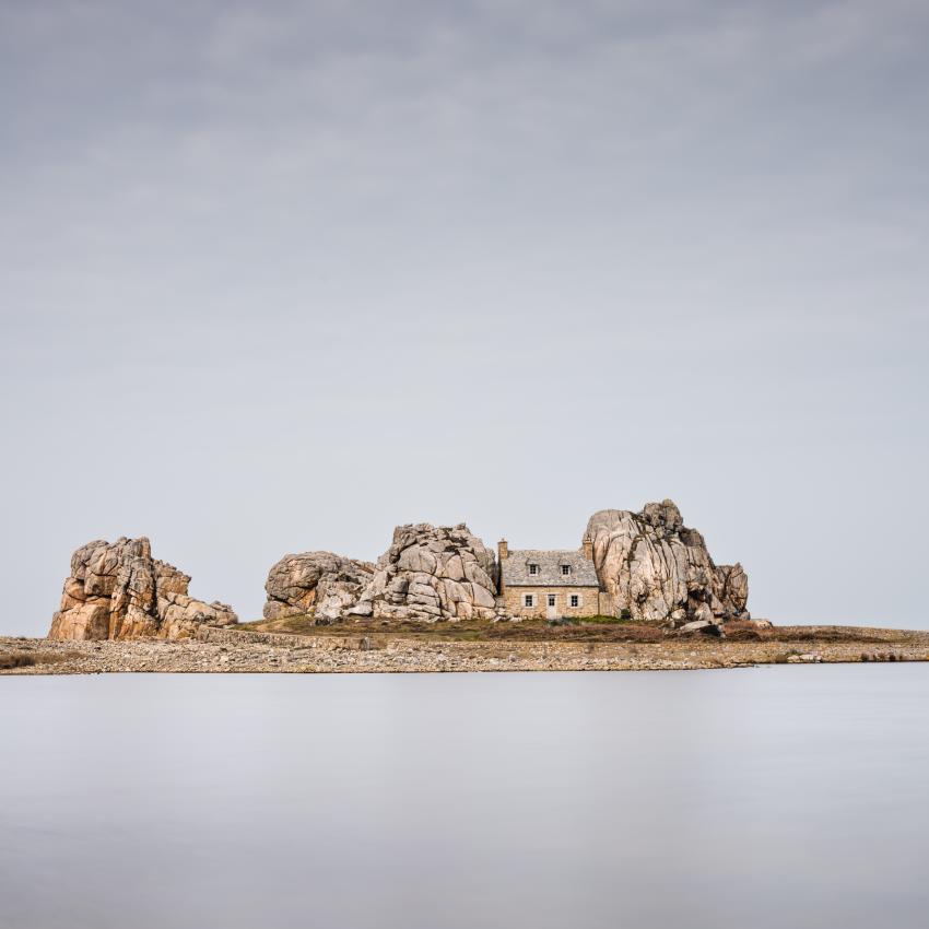 'The Squashed House'. A house sandwiched between two rocks on a spit of land on the coast of Brittany, France. Thankfully, it was a very calm day when I took this photograph, which emphasised the pink granite in the otherwise tranquil setting. © Robert Bolton, United Kingdom, Shortlist, Open Competition, Architecture, 2023 Sony World Photography Awards