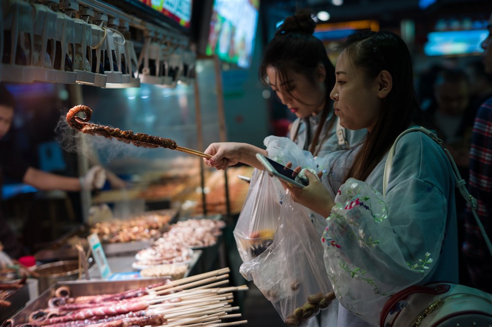 epa06370346 A woman buys a barbecued octopus tentacle at a night market stall in Shenzhen, China, 05 December 2017 (issued 06 December 2017). The night market is situated in the Dongmen Commercial Area, one of the oldest commercial centers in Shenzhen. The night market offers anything from barbecued squids, pig knuckles, lamb skewers, garlic oysters to fried crayfish, chicken wings and insects on a stick. EPA-EFE/STRINGER
