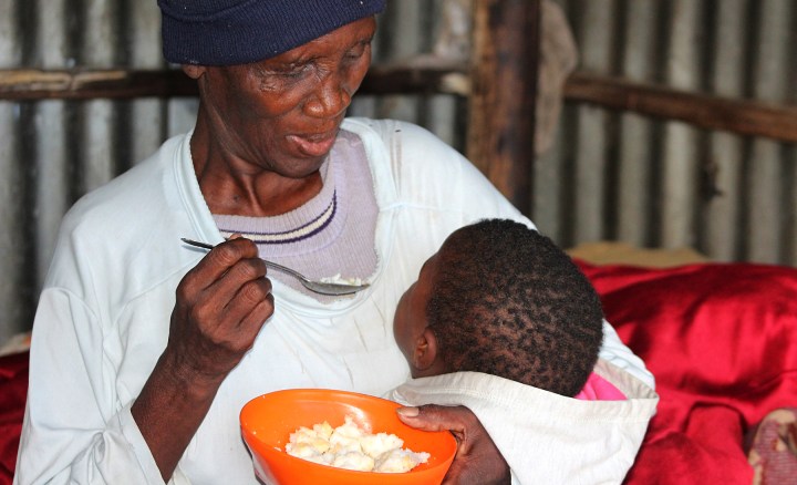 Nombembe Nolusapho Olivia (70),  one of the old age grant beneficiaries, feeding her granddaughter with the day before's food (pap) at Chris Hani Park in Mthatha West,  Eastern Cape. (Photo: Hoseya Jubase)