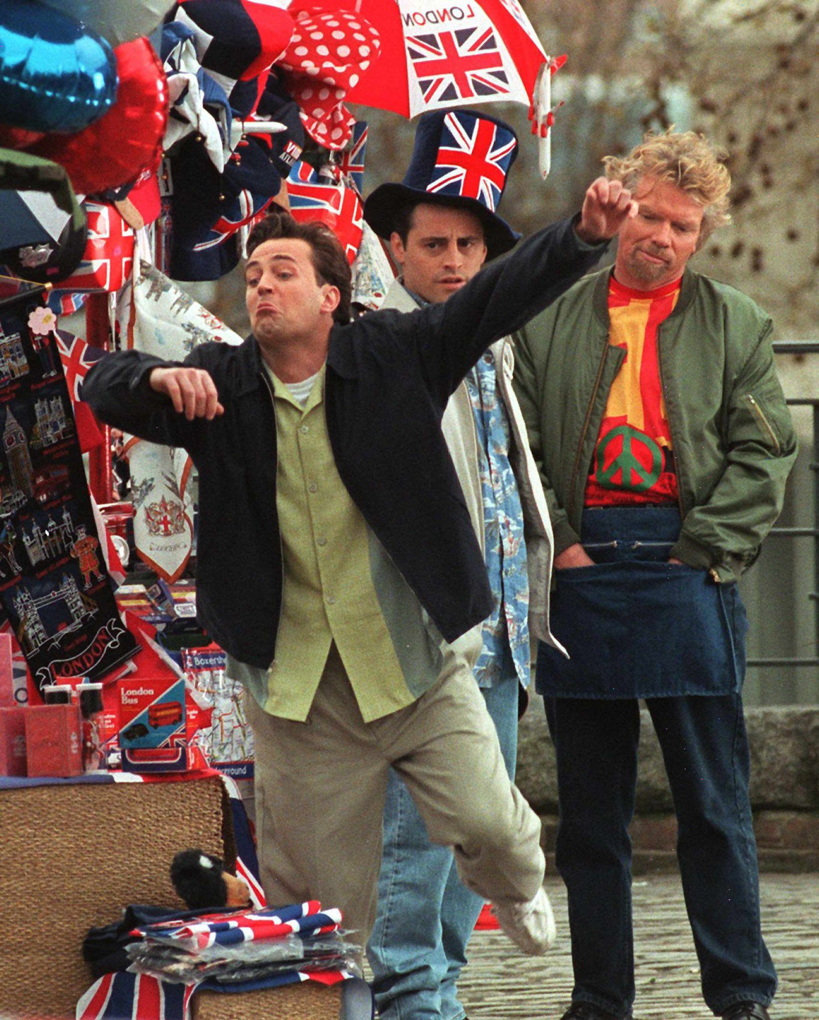 LOM04-19980327-LONDON: American actor Matthew Perry (L), who plays Chandler in the American show 'Friends', trips during filming at the Tower of London watched by Matt Le Blanc (C) who plays Joey and Virgin airline boss Richard Branson (R), who plays a souvenir seller, 27 March. The hit American show is in Britain to film the cliffhanger final episode of the current series in which actor David Schwimmer's character Ross is due to marry Emily, played by British star Helen Baxendale. EPA PHOTO Gerry PENNY